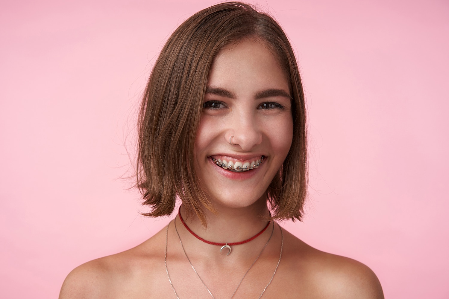 close up of young cheerful brown eyed brunette female with bob haircut looking happily at front with charming smile isolated over pink wall